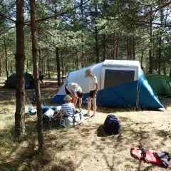 Rodzina rozbija obóz w lesie. Dzieci pomagają przy namiotach, zastanawiając się, jaki śpiwór na lato będzie najlepszy.