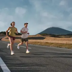 Para biegnie po asfaltowej drodze na tle malowniczego krajobrazu z górą w oddali. To idealne miejsce na bieganie w terenie.
