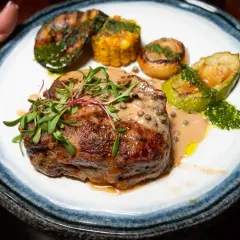 Un succulent filet mignon barbecue, nappé d'une sauce crémeuse aux poivres, accompagné de légumes grillés et de maïs.