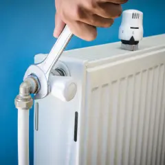 Réparation d'un radiateur bruyant. Une clé serre un raccord, peut-être pour arrêter l'eau qui coule.