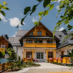 Piękny dom z żółtymi zdobieniami i balkonami, otoczony zielenią. Idealne miejsce na wypoczynek, odkryj tylicz atrakcje!