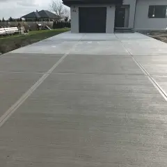 Nowy podjazd z beton stemplowany, z wyraźnymi fugami, prowadzi do nowoczesnego domu z szarą bramą garażową.
