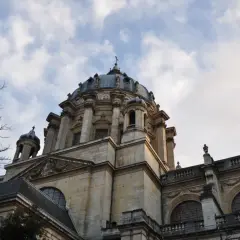 Dôme majestueux de l'église du Val-de-Grâce, se détachant sur un ciel nuageux. L'architecture baroque est impressionnante.