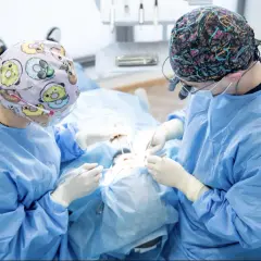 Chirurdzy stomatologiczni wykonują zabieg augmentacji kości, precyzyjnie pracując w jamie ustnej pacjenta.