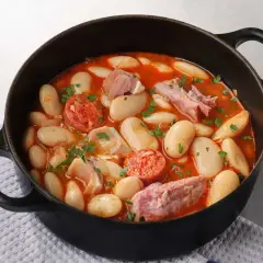 Judiones de la granja en cazuela negra, con chorizo, tocino y perejil picado. Un plato reconfortante y lleno de sabor.
