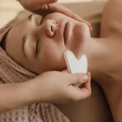 Un viso rilassato riceve un massaggio con pietra gua sha, una tecnica che serve a migliorare la circolazione e il drenaggio linfatico, donando luminosità.