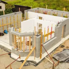 Budowa domu energooszczędnego z bloczków betonowych i białych płyt izolacyjnych. Widać zbrojenia i elementy konstrukcyjne.