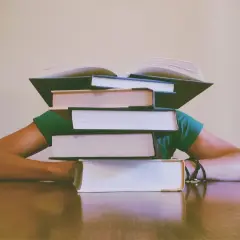 Stos książek przygniata głowę studenta. Jak napisać dyskusję w pracy magisterskiej? Czas na naukę!
