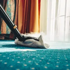 Dampfreiniger reinigt einen blauen Teppich mit Muster. Dampf steigt auf, während die Düse über den Boden gleitet.