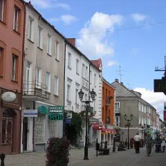 Ulica w Polsce, z kamienicami po obu stronach. Widać szyldy sklepów, m.in. "Jubiler" i "Casio". Kierunkowy 86 w Polsce.