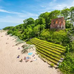 Słoneczna plaża w Trzęsaczu z ruinami kościoła na klifie. Piasek, morze i zielone wzgórze tworzą malowniczy krajobraz.