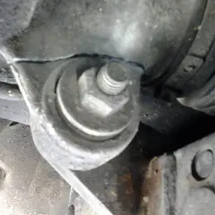 Soporte metálico con un perno hexagonal sujetando una pieza del motor, cerca de un componente que podría ser parte del volante de dirección.