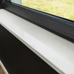 Jasny parapet z konglomeratu z widocznymi plamami, obok czarnej ściany i okna.