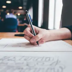 Dłoń pisze na papierze, zastanawiając się, czy odpowiedź na pozew doręcza się pełnomocnikowi.