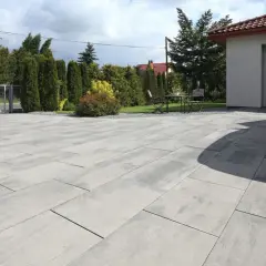Nowoczesny podjazd z szarej kostki brukowej przed domem z garażem i białym samochodem.