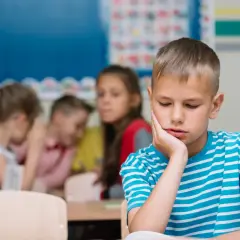 Un bambino solo in classe, con la mano sul viso, mentre altri bambini ridono e parlano tra loro. Sembra che mia figlia non abbia amici.