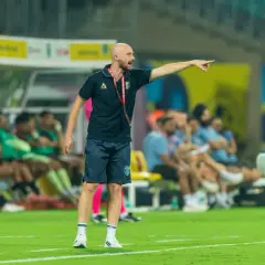 Tomasz Tchórz, trener, wskazuje kierunek na boisku. Za nim siedzą zawodnicy na ławce rezerwowych.