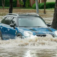 Niebieski Mini Cooper przedziera się przez powódź. Ubezpieczenie GAP przy zakupie za gotówkę chroni przed stratami w takich sytuacjach.