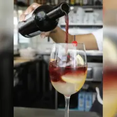 Rotwein wird in ein Glas mit Eis, Zitrone und Kirsche gegossen. Perfekt für rotwein im sommer.