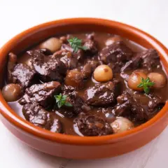 Herzhaftes Spezzatino di manzo mit kleinen Zwiebeln und Kräutern in einer Terrakotta-Schale.
