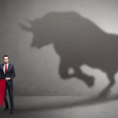 Un hombre con traje y corbata roja sostiene una tela roja, mientras la sombra de un toro irrumpe en la pared. ¿Qué significa soñar con toros?