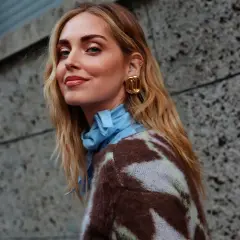 Mujer con cabello rubio ondulado y cortes de pelo media melena modernos, luciendo un suéter estampado y pendientes dorados.