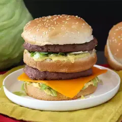 Burger double étage avec fromage, laitue et sauce sur une assiette blanche.