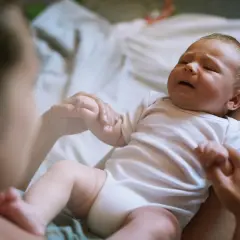 Płaczący noworodek na kolanach mamy. Jego twarz wyraża oznaki głodu, a rączki szukają pocieszenia.