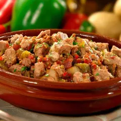 Un plat d'axoa de veau mijoté avec des poivrons et des oignons, garni de persil frais, dans un bol en terre cuite.