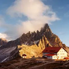 Sonnenuntergang an einer Berghütte. Die schroffen Gipfel der Dolomiten ragen hinter dem Gebäude auf. Hier könnte man gut zwei Wochen auf der Alm arbeiten.