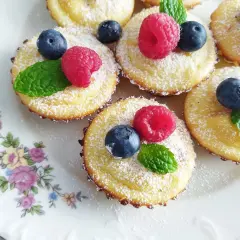 Urocze mini serniczki posypane cukrem pudrem, ozdobione malinami, borówkami i listkami mięty. Idealne na deser.