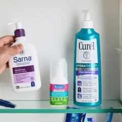 Dłoń sięga po balsam Sarna, by złagodzić swędzące plecy. Obok spray Benadryl i balsam Curél.