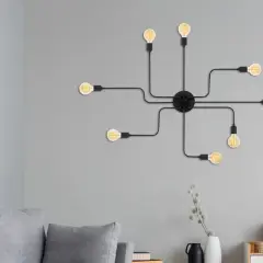 Un aplique de pared negro con siete bombillas Edison, que parece una araña moderna, ilumina la pared gris sobre un sofá.