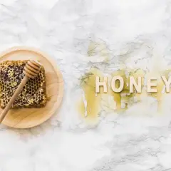 Plaster miodu z drewnianym mieszadełkiem na talerzyku i napis "HONEY" z miodu na marmurowym tle.