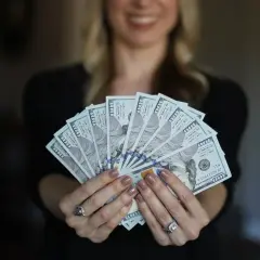 Uśmiechnięta kobieta trzyma wachlarz banknotów 100-dolarowych. Czy Vivus wyplaca w sobotę?