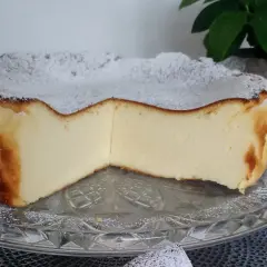 Puszysty sernik z mlekiem, oprószony cukrem pudrem, prezentuje się apetycznie na szklanej paterze.