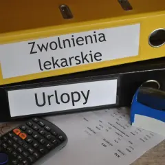 Segregator "Zwolnienia lekarskie" i "Urlopy" obok kalkulatora i pieczątki. Dokumenty gotowe do archiwizacji, może to być kod c na l4.