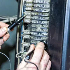 Ręce sprawdzają bezpieczniki w skrzynce elektrycznej. Czy bezpiecznik może się zepsuć? Tak, dlatego warto je kontrolować.