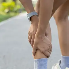 Un corridore si tiene la gamba, con le mani che stringono il polpaccio. Il tutore al polso è visibile. Il tutore mi fa male.