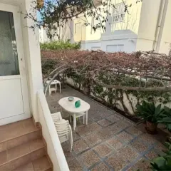 Patio con mesa y sillas bajo una pérgola cubierta de enredaderas secas. Un gran cortijo se vislumbra al fondo.