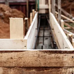 Drewniana szalunkowa konstrukcja przygotowana pod fundament pod ogrodzenie. W środku widoczna zbrojenie.