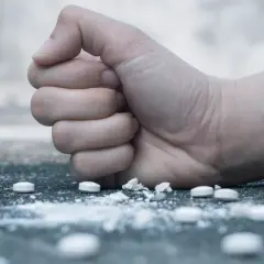 Zaciśnięta pięść nad białym proszkiem i tabletkami, symbolizująca walkę z nałogiem, np. flakka.