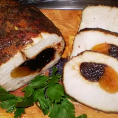 Schab ze śliwką i morelami, pieczony, pokrojony w plastry, z gałązką natki pietruszki.