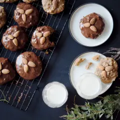 Schokoladenüberzogene Elisenlebkuchen mit Marzipan und Mandeln auf einem Gitter, daneben Milchgläser und Tannenzweige.