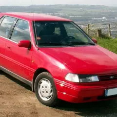 Czerwony Hyundai Pony stoi na polnej drodze, z widokiem na krajobraz w tle.