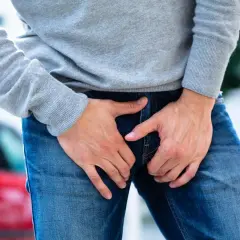 Un homme tient ses mains sur son entrejambe, suggérant une douleur pelvienne.