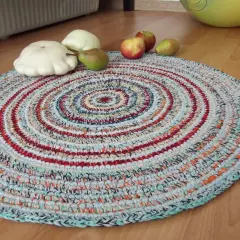 Tappeto uncinetto rotondo con fantasie a spirale multicolore. Sopra, zucche bianche, una pera e mele rosse.