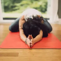 Mujer en postura de niño en esterilla roja, practicando una de las 20 posturas de yin yoga.