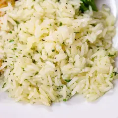 Fluffy white rice with flecks of green herbs, perfect for a simple rice seasoning recipe. A side of grilled chicken is visible.