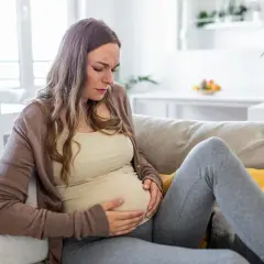 Ciężarna kobieta z grymasem bólu na twarzy, trzymająca się za brzuch. Może to być objaw cholestazy ciążowej.
